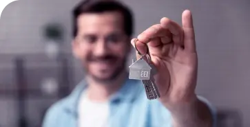 A imagem mostra um homem branco segurando as chaves de uma casa e sorrindo. Ele veste camiseta branca e camisa azul.